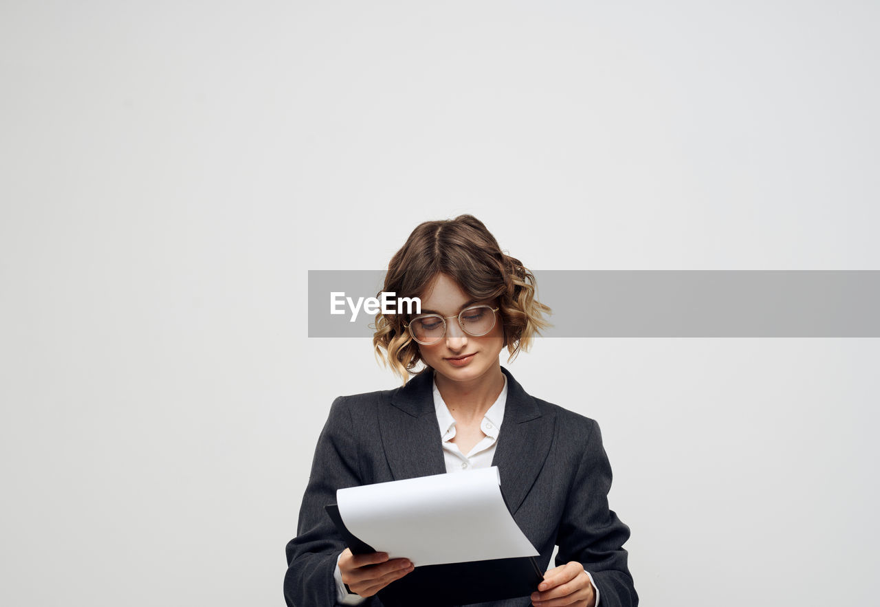 business, adult, one person, copy space, businesswoman, women, indoors, studio shot, portrait, formal wear, business finance and industry, front view, smiling, communication, female, occupation, holding, young adult, working, office, professional occupation, eyeglasses, waist up, standing, looking, white background, digital tablet, corporate business, happiness, hairstyle, brown hair, white-collar worker, glasses, conversation, computer, technology, person, laptop, gray, sitting, success, emotion, looking at camera