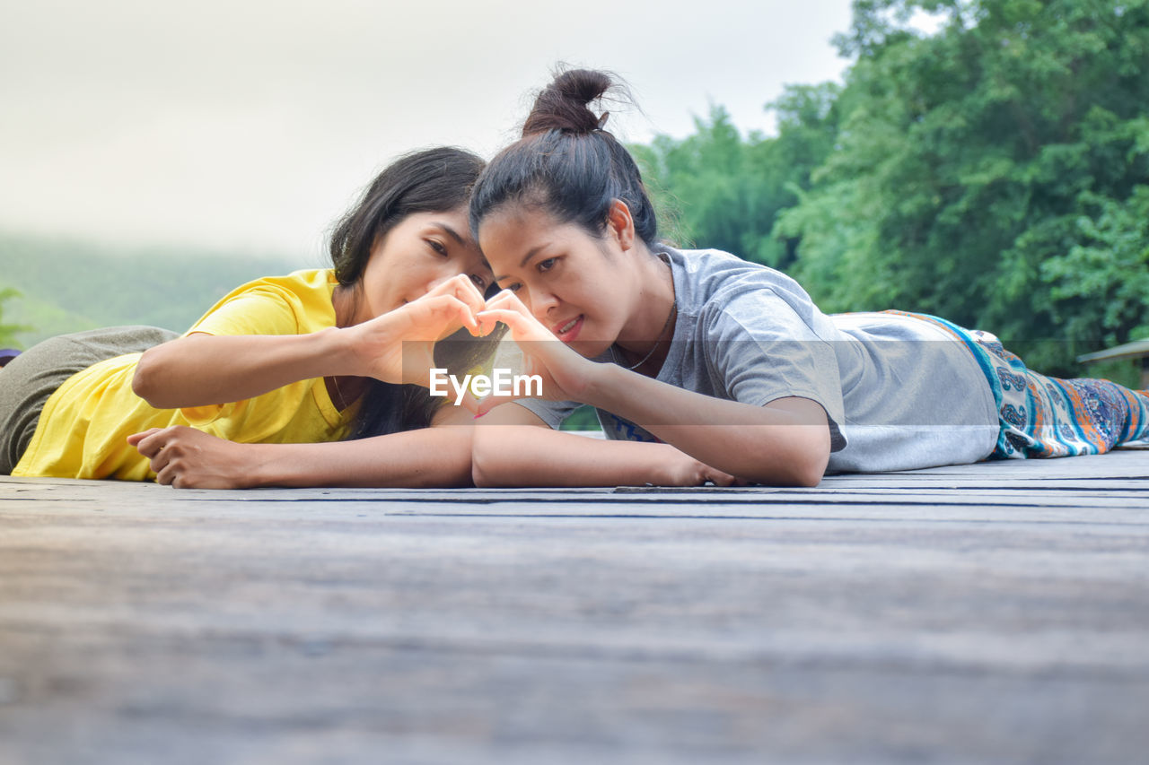 Smiling women making heart shape lying on wood