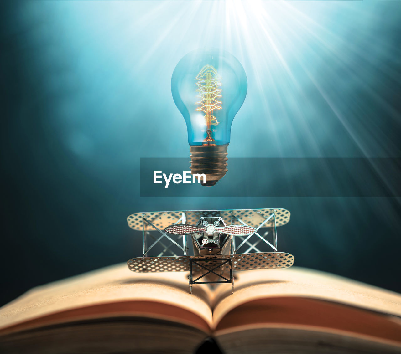 Digital composite image of illuminated light bulb over model airplane and book