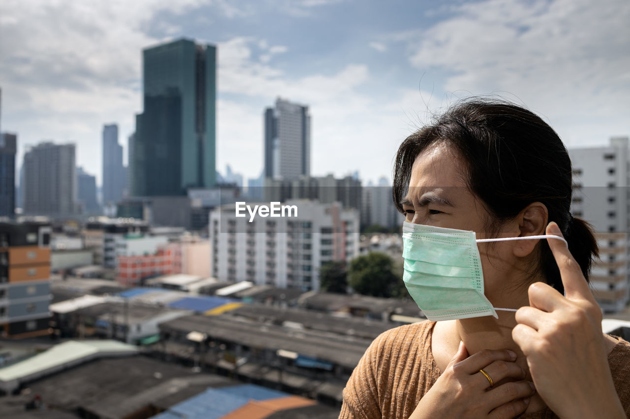 Woman wearing mask looking away against buildings