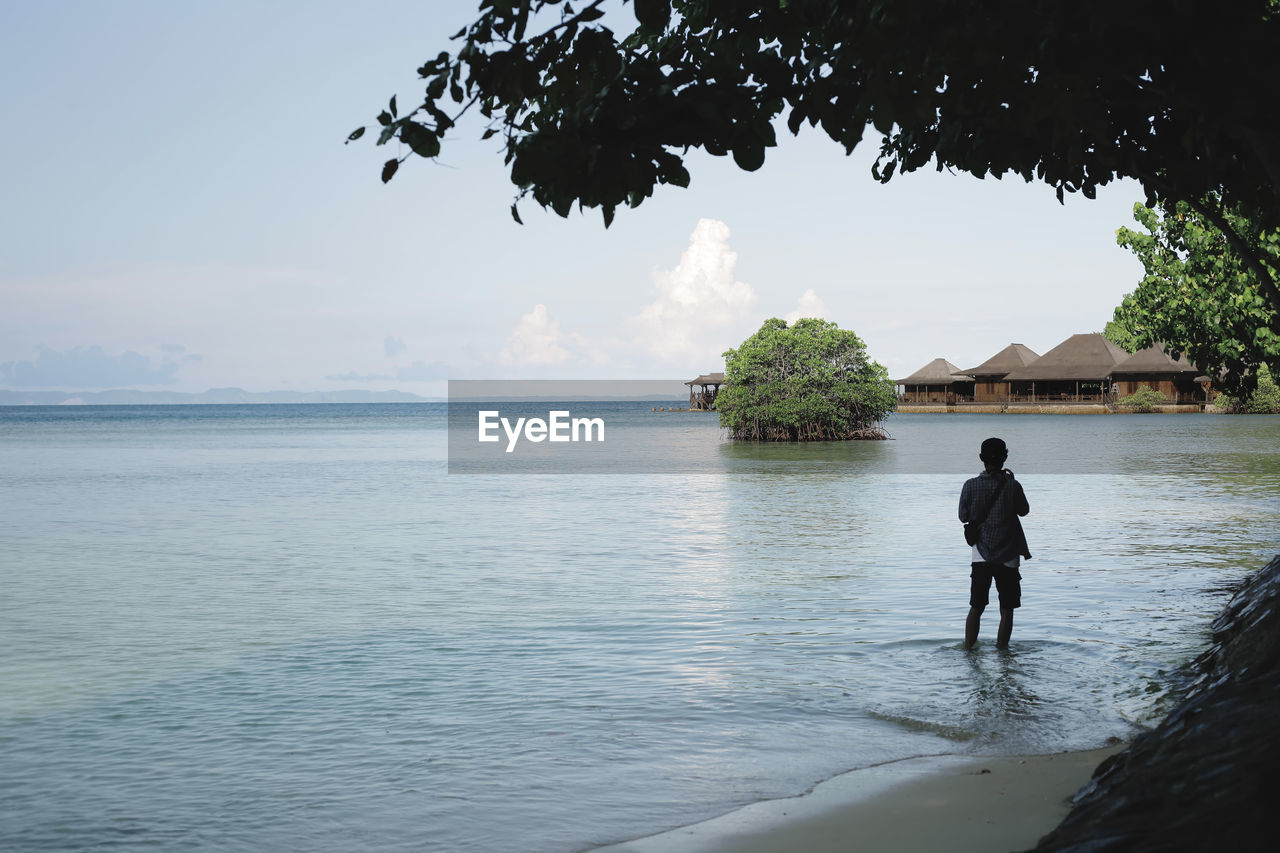 Rear view of man standing in sea against sky