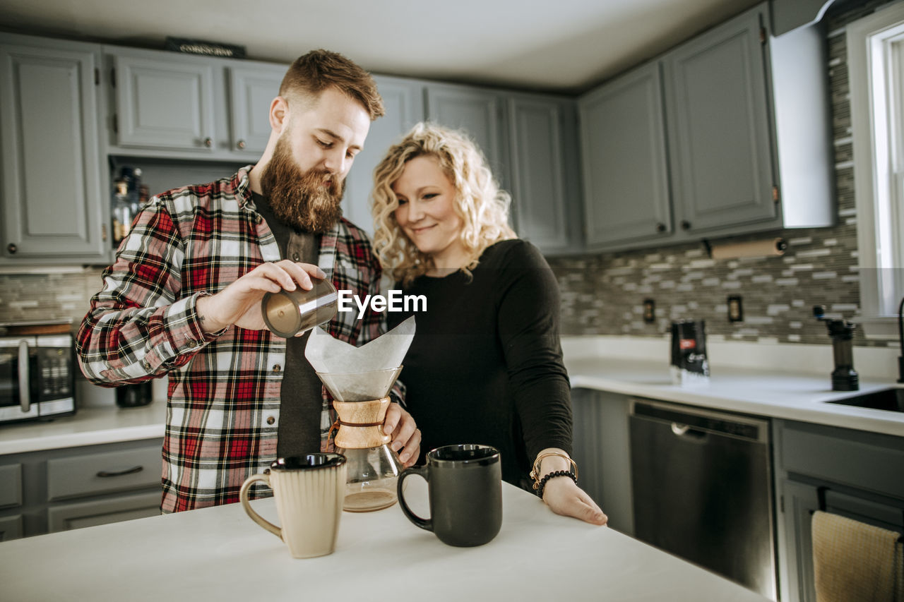 Man with beard and woman make over coffee together in their kitchen