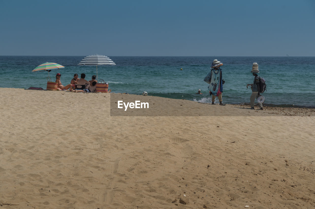 Vendors selling hats while people resting at beach