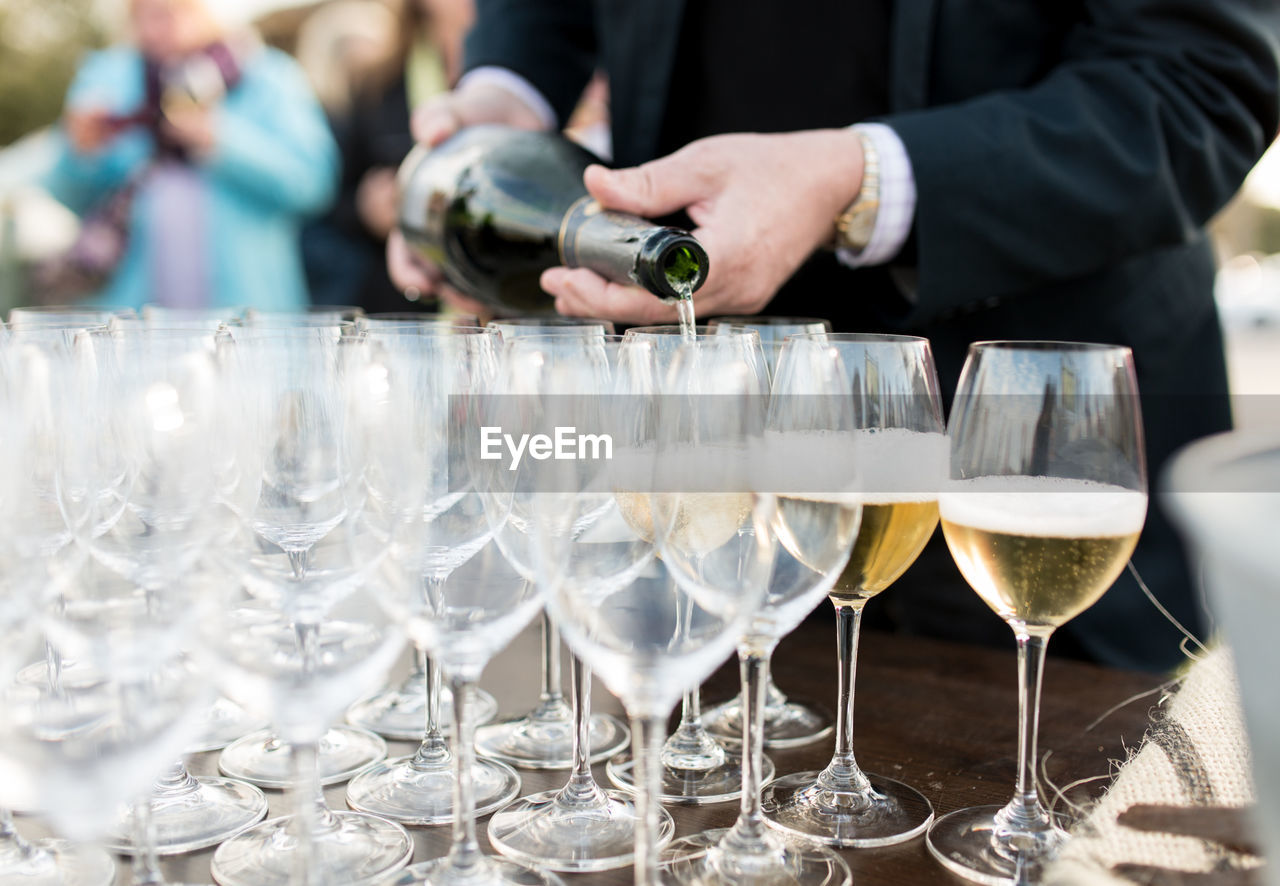 Midsection of man pouring wine in glasses on table