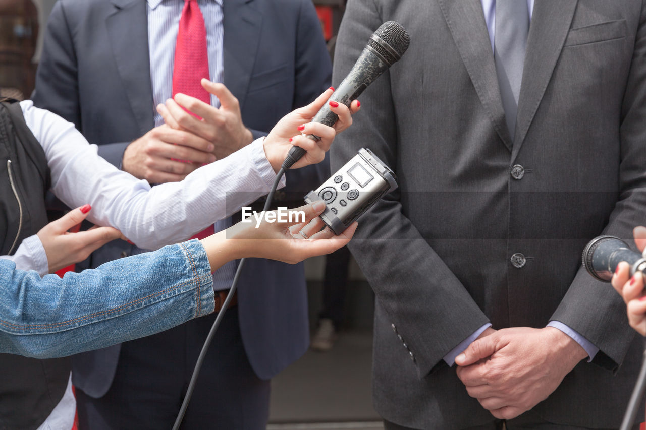 Cropped image of people holding microphone while interviewing business people