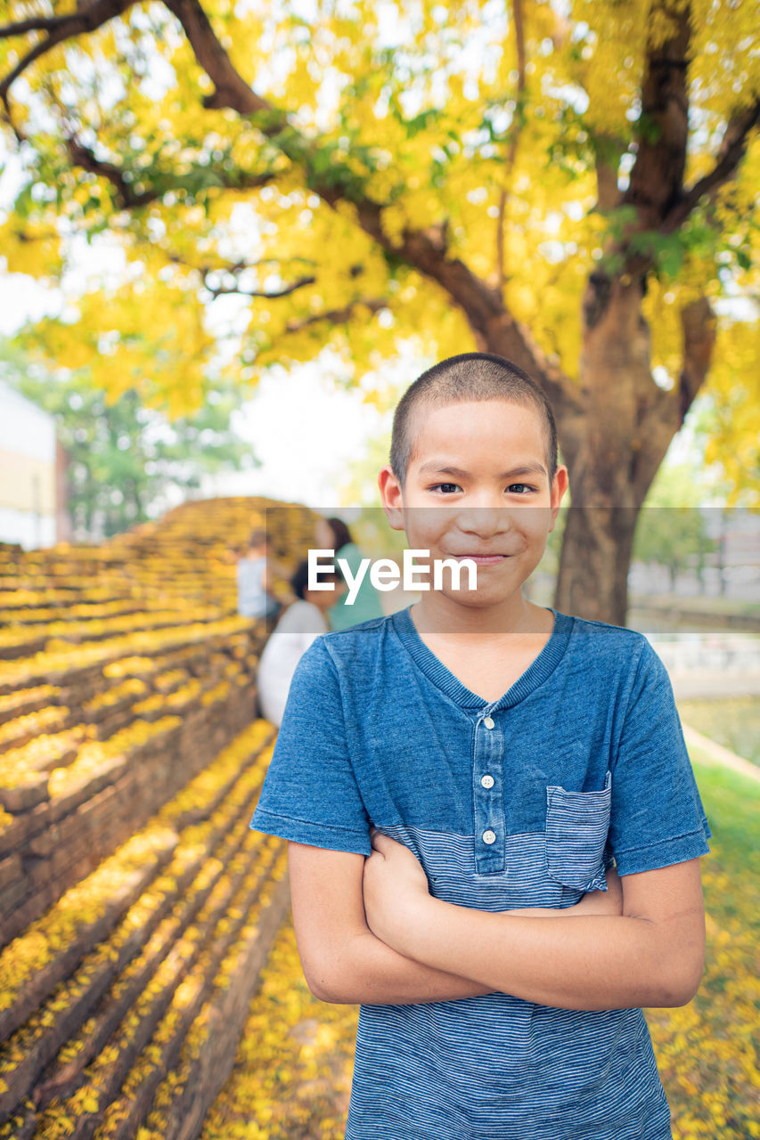 PORTRAIT OF SMILING BOY STANDING AGAINST TREE