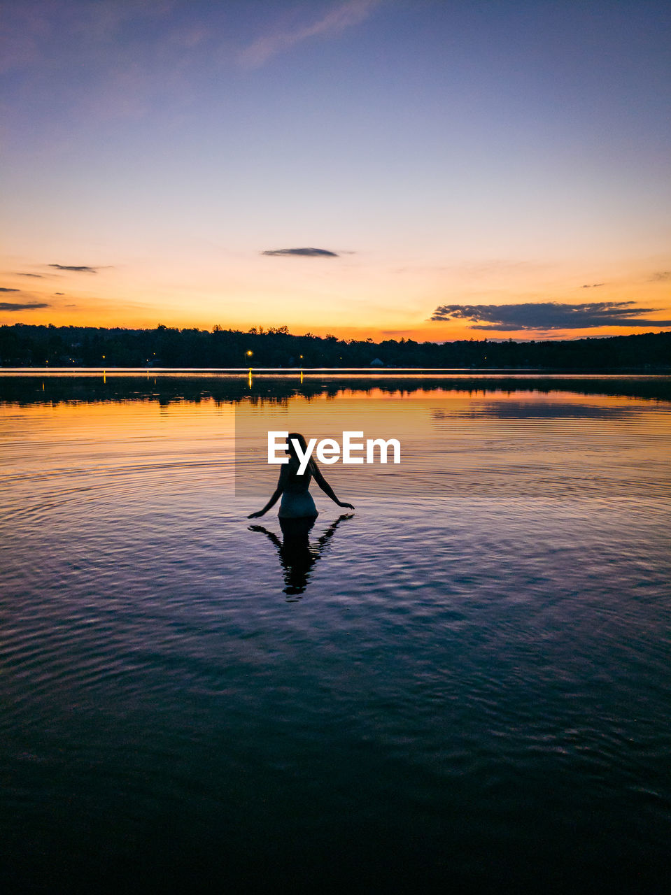 Silhouette man in swimming pool by lake against sky during sunset