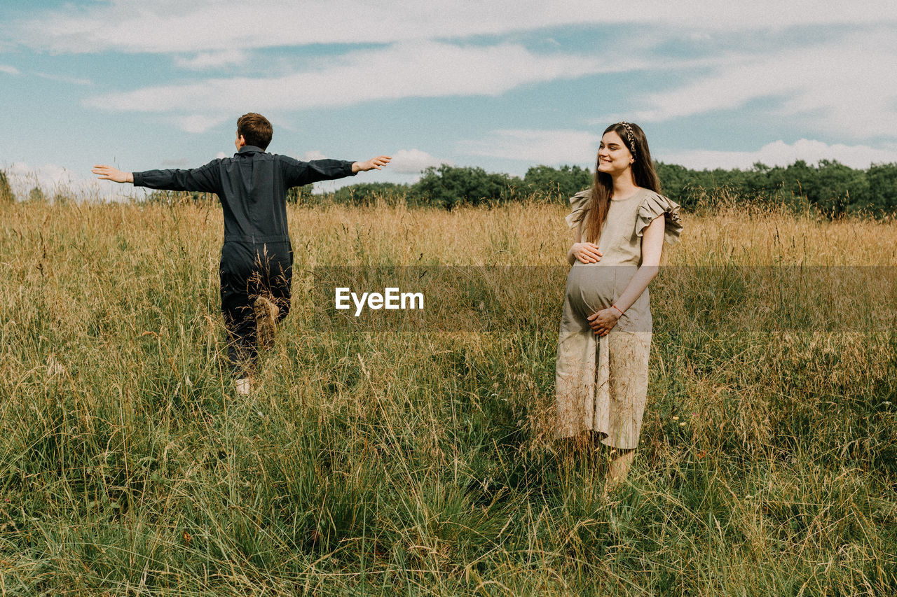 Pregnant woman with boyfriend running on grassy field