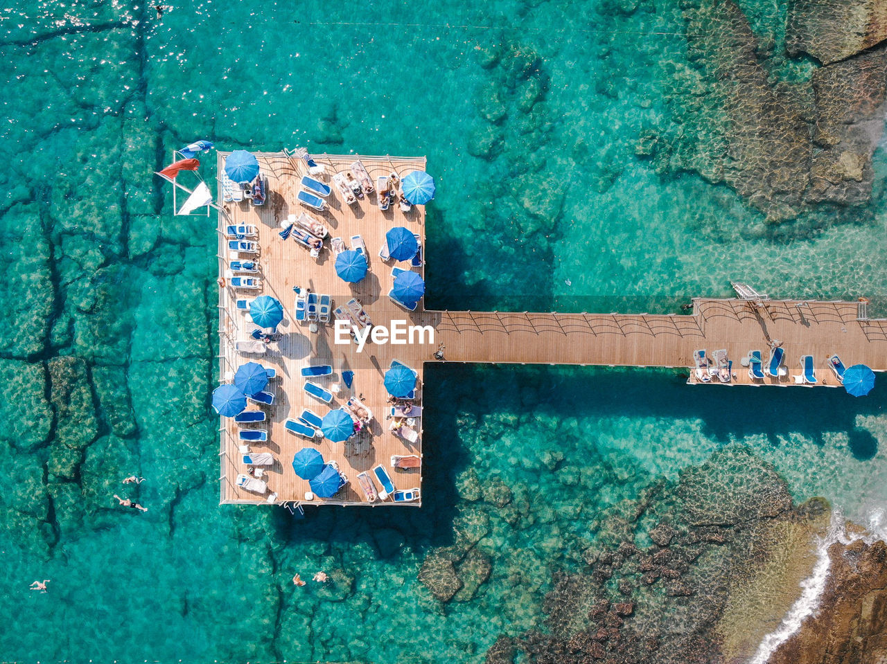 Drone view of lounge chairs and parasols on pier over sea