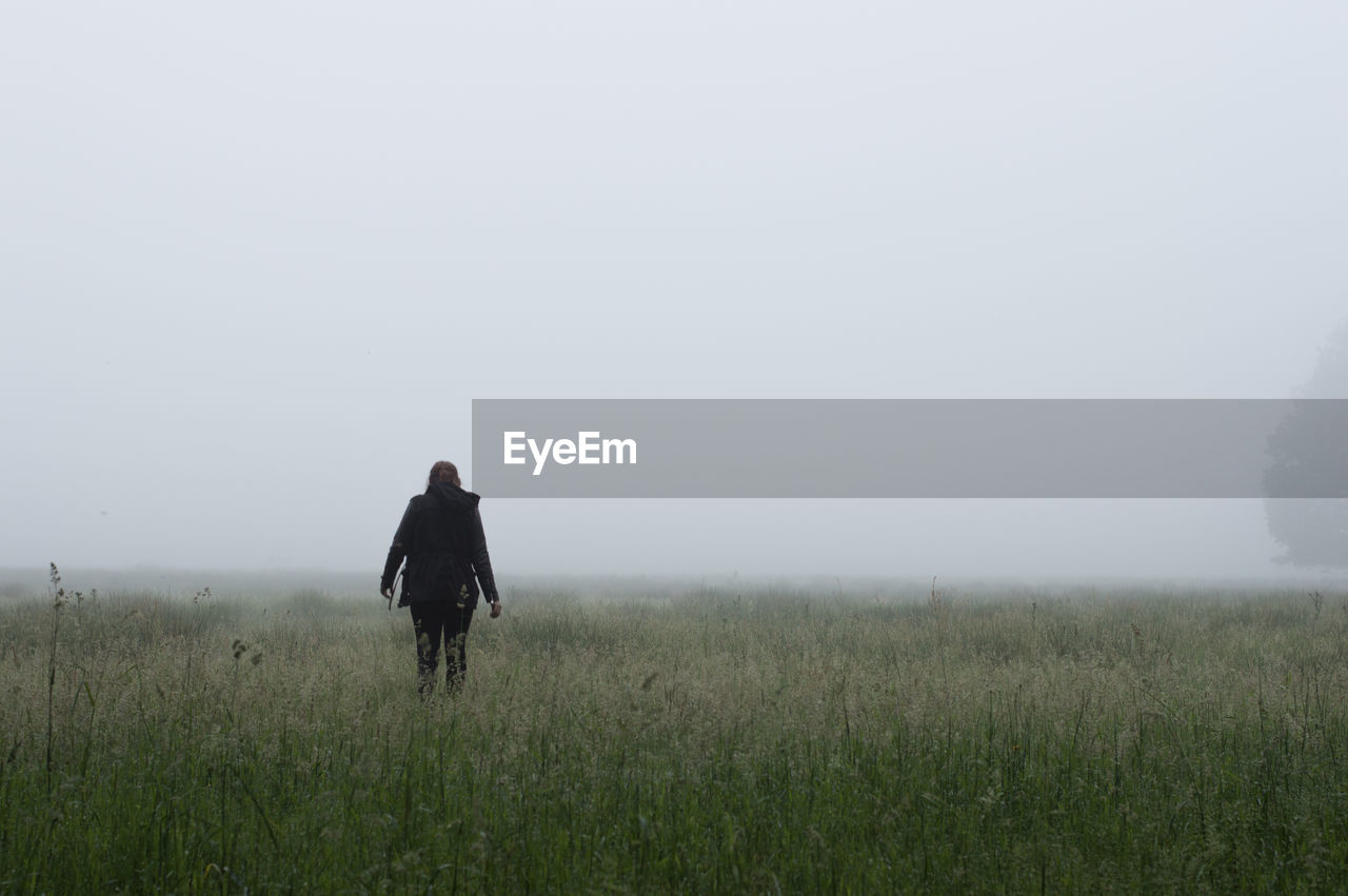 Rear view of woman walking on grassy field in foggy weather