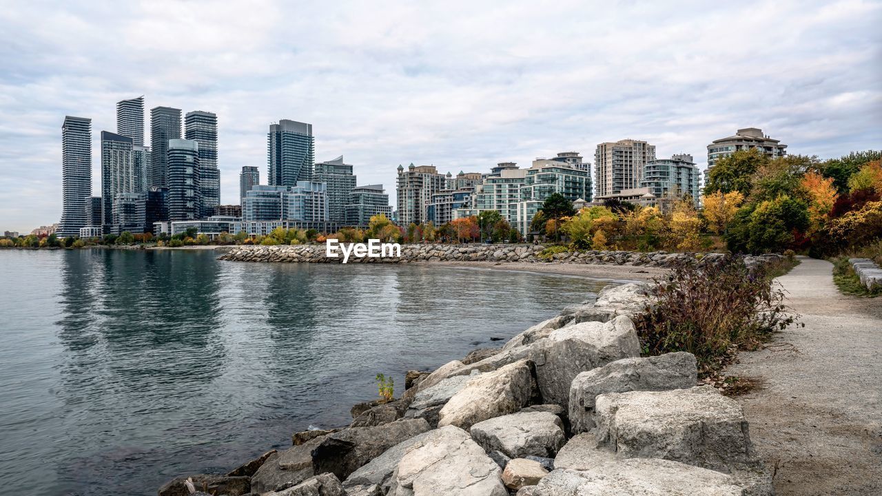 Buildings by river against cloudy sky during autumn