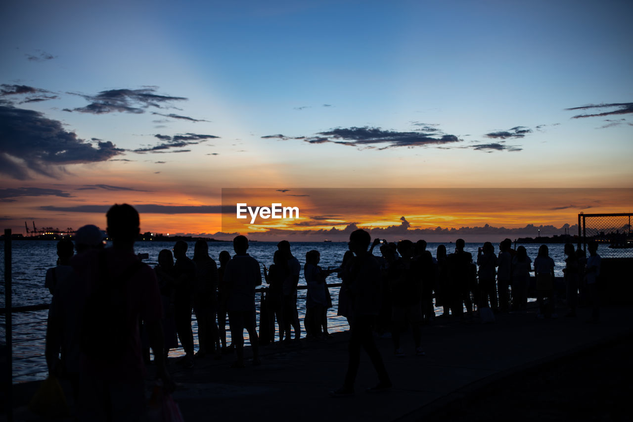 Silhouette people at beach against sky during sunset