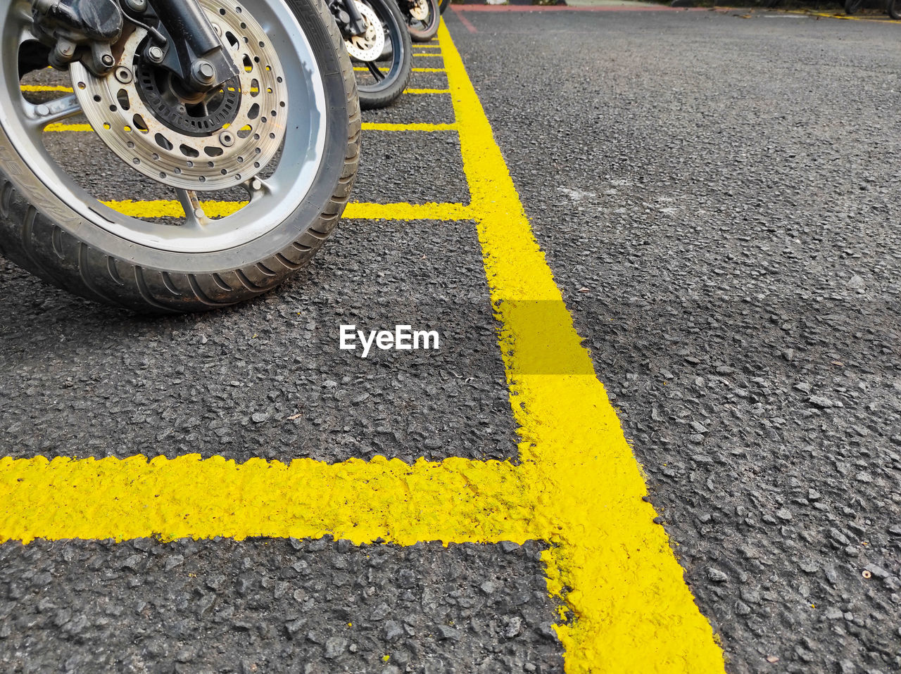transportation, road, yellow, road marking, asphalt, symbol, marking, sign, mode of transportation, street, city, tarmac, road surface, day, tire, wheel, lane, vehicle, no people, double yellow line, land vehicle, outdoors, motor vehicle, auto part, high angle view, communication, dividing line, car, bicycle