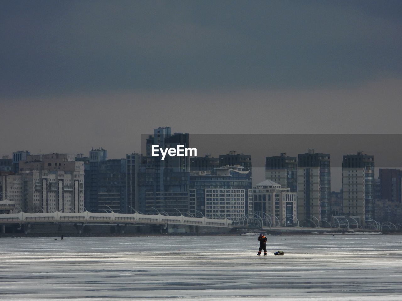 Man walking on frozen sea against buildings in city