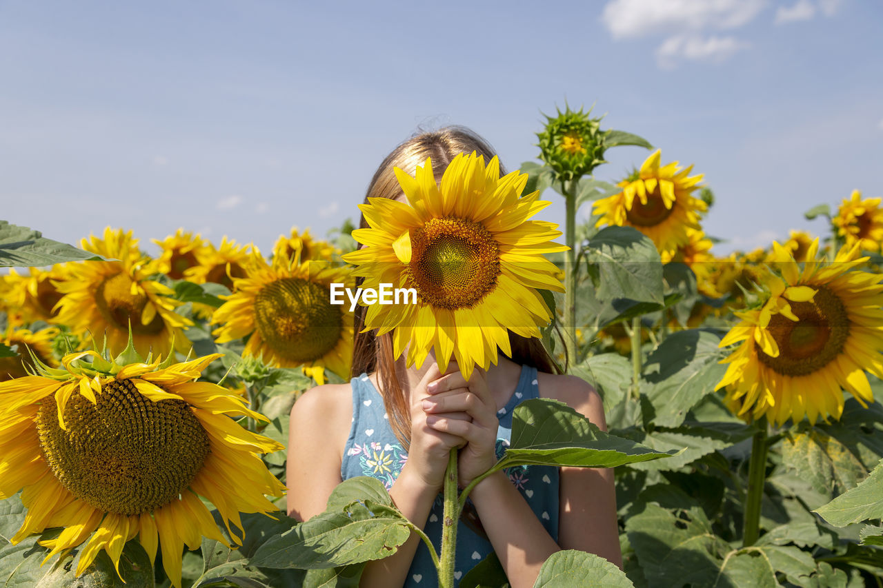 Girl holding sunflower in front of her face in the field. generation z.