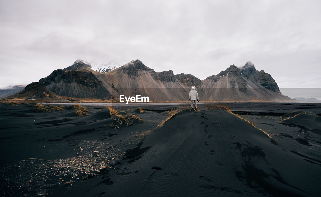 Rear view of man standing on land against mountains and sky