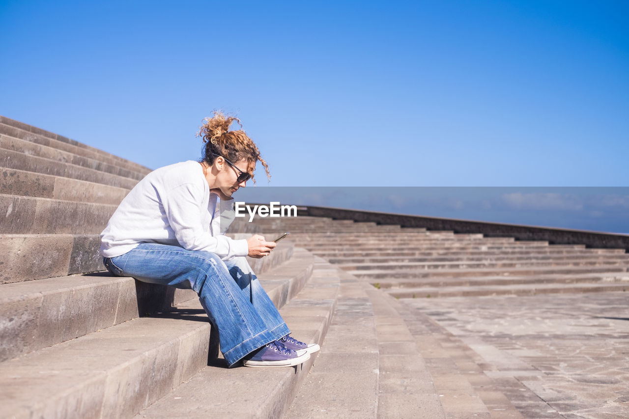Woman sitting on steps against blue sky
