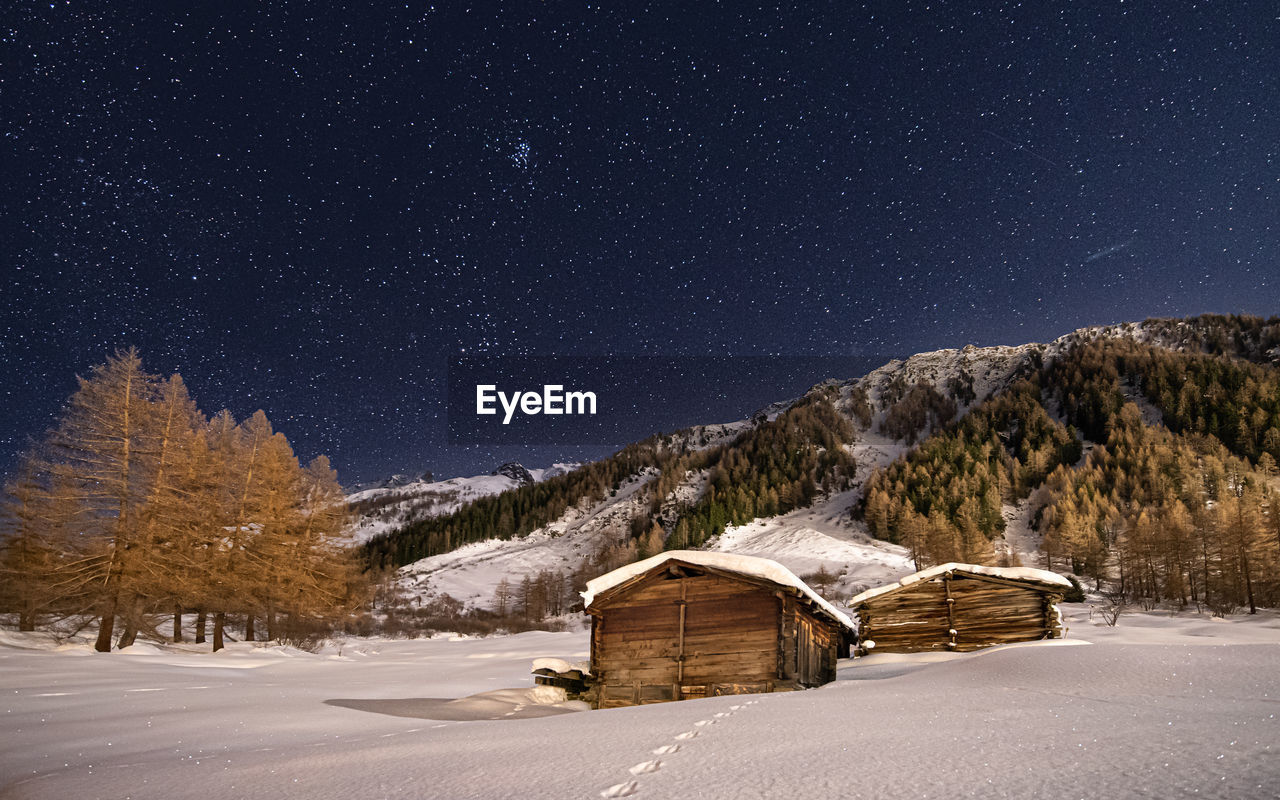 Scenic view of snowcapped landscape with wooden cottages against sky at night