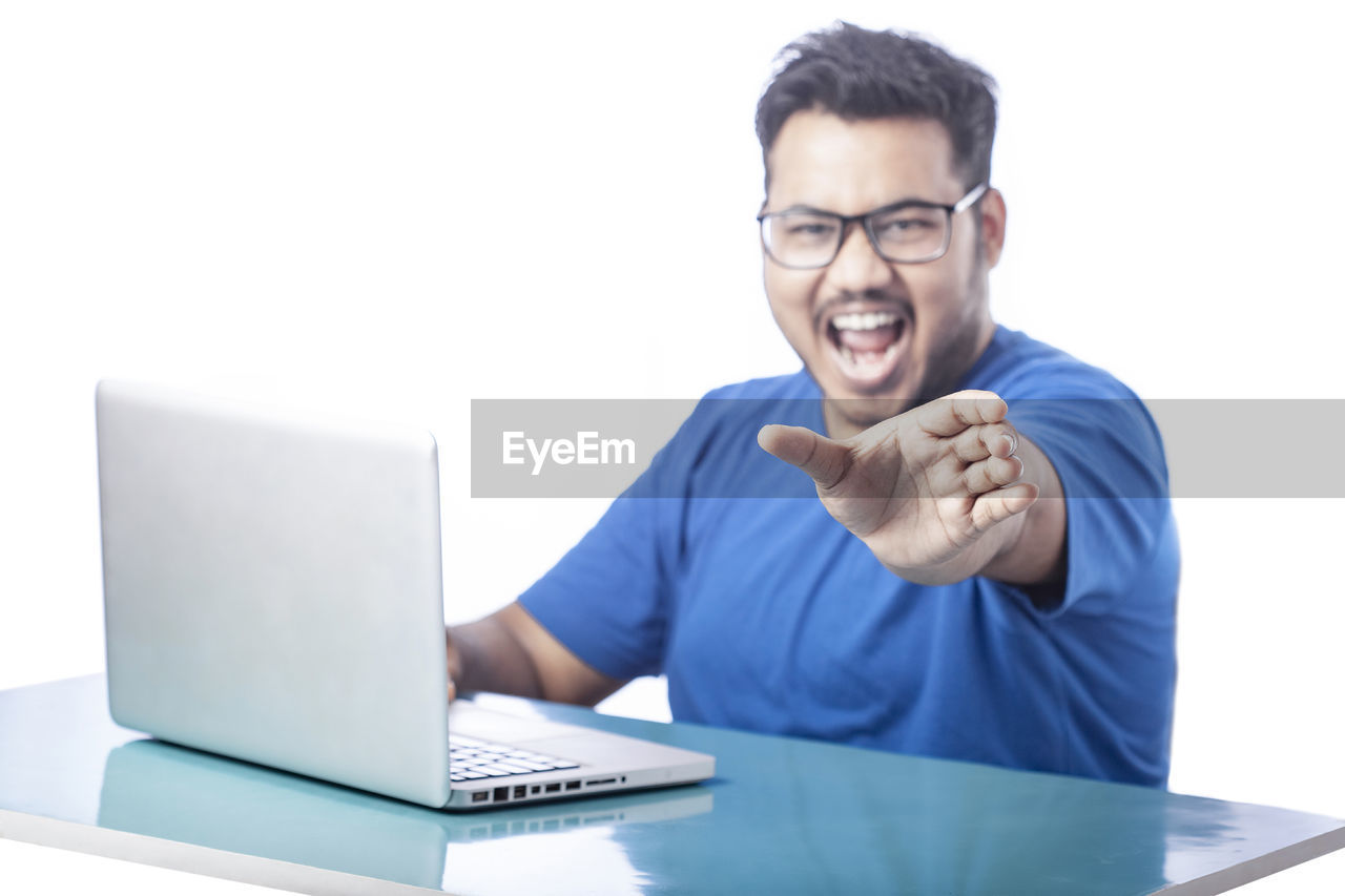 computer, technology, laptop, adult, one person, wireless technology, communication, eyeglasses, men, using laptop, business, glasses, businessman, happiness, smiling, emotion, indoors, young adult, writing, internet, cheerful, white background, furniture, office, casual clothing, portrait, looking, computer network, person, table, desk, computer equipment, white-collar worker, sitting, working, relaxation, positive emotion, studio shot, e-mail, occupation, front view, place of work, copy space, cut out, lifestyles, typing, button down shirt, conversation, corporate business, business finance and industry