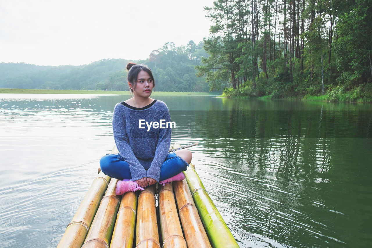 Full length of woman sitting on wooden raft in lake