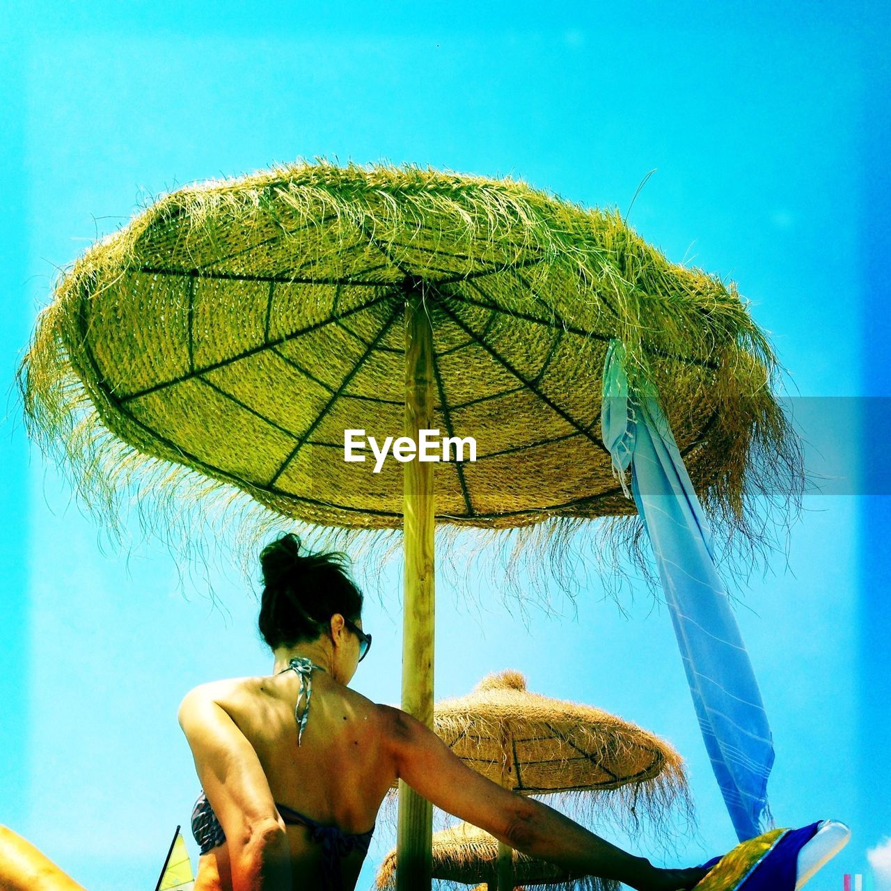 Rear view of woman under thatched roof parasol against sky