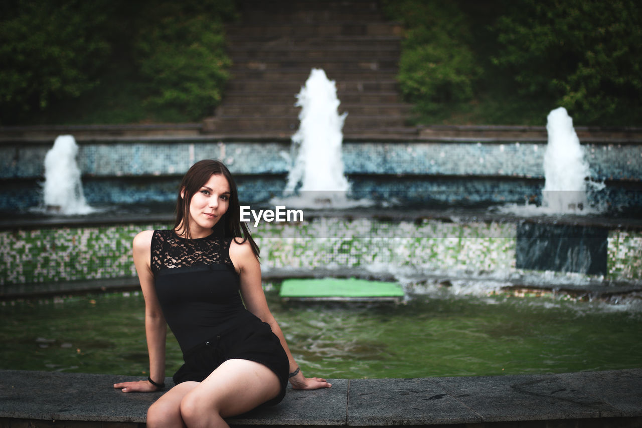 Portrait of young woman sitting against fountain