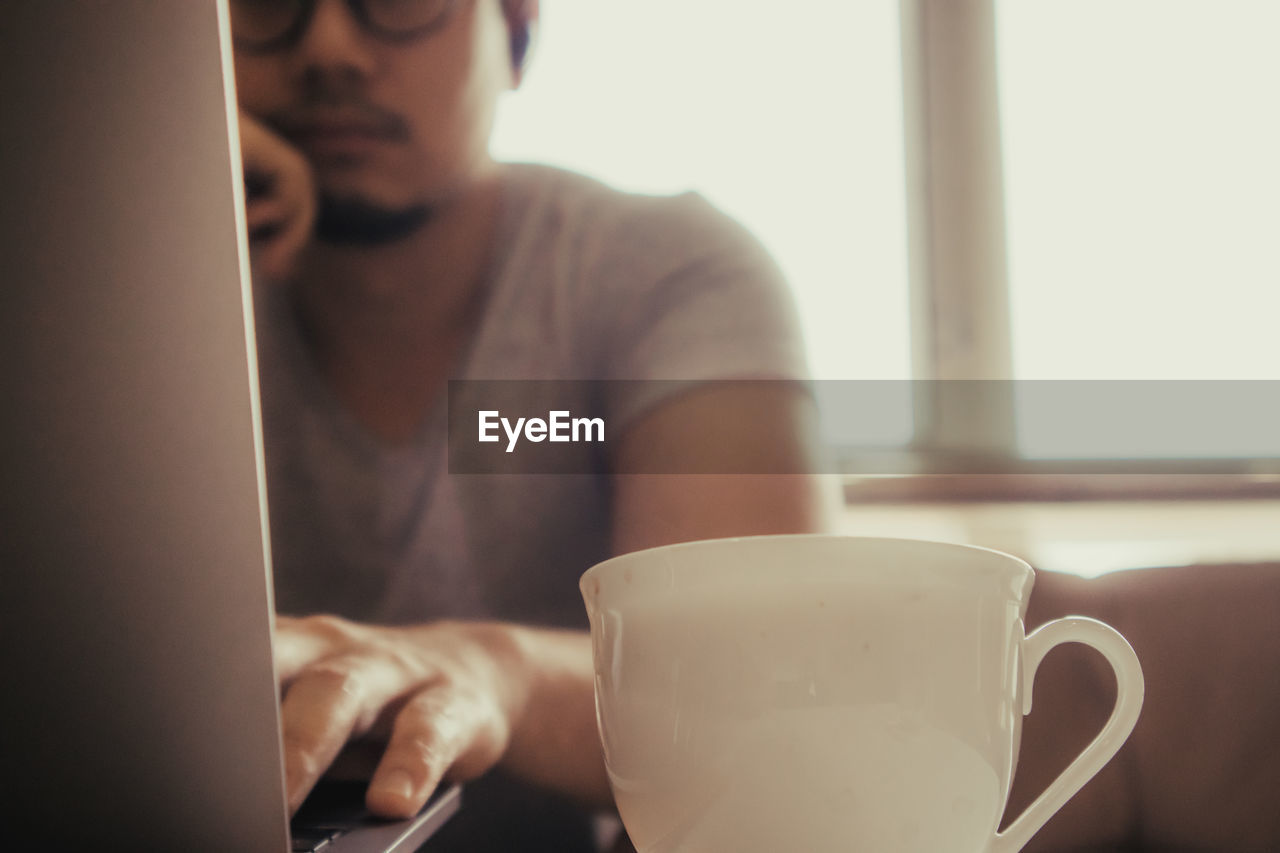 Man using laptop by coffee cup at desk