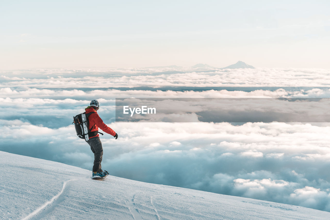 Snowboarder riding down mountain at sunset above clouds