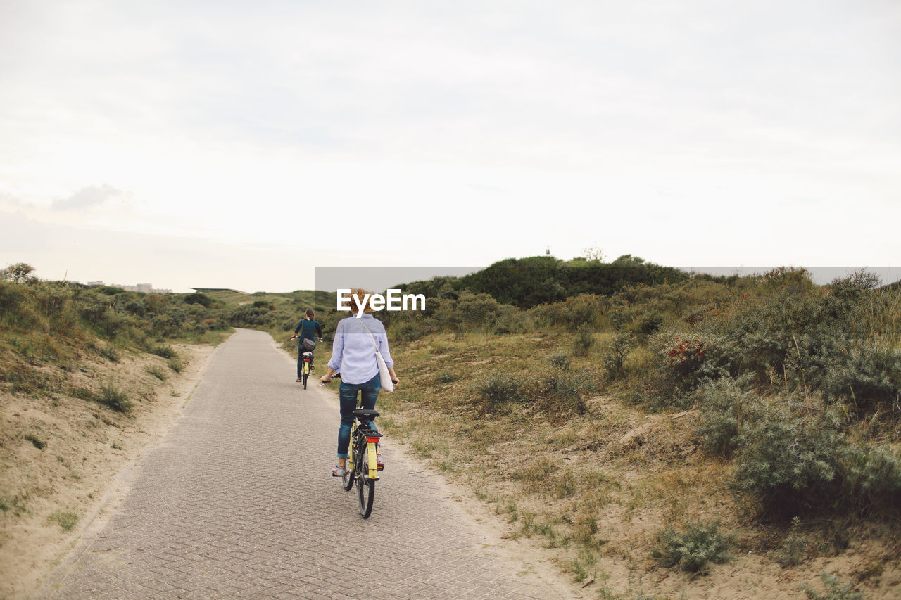 Rear view of friends riding bicycles on road against sky