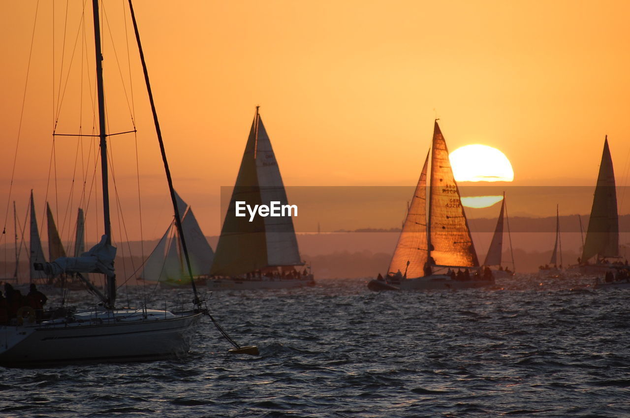 Sailboats sailing in sea against orange sky