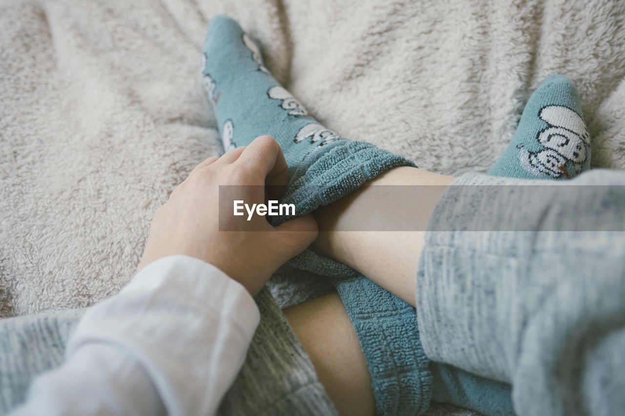 Low section of woman wearing socks resting on bed at home