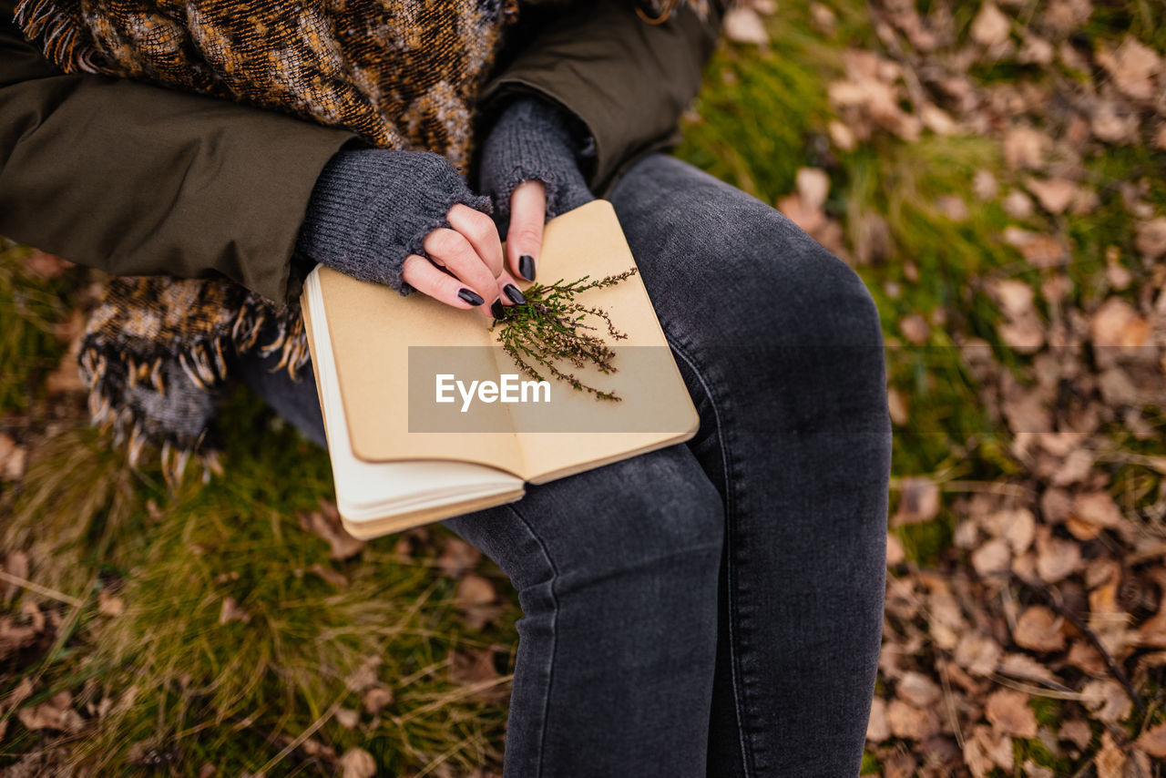 MIDSECTION OF WOMAN READING BOOK AGAINST TREE