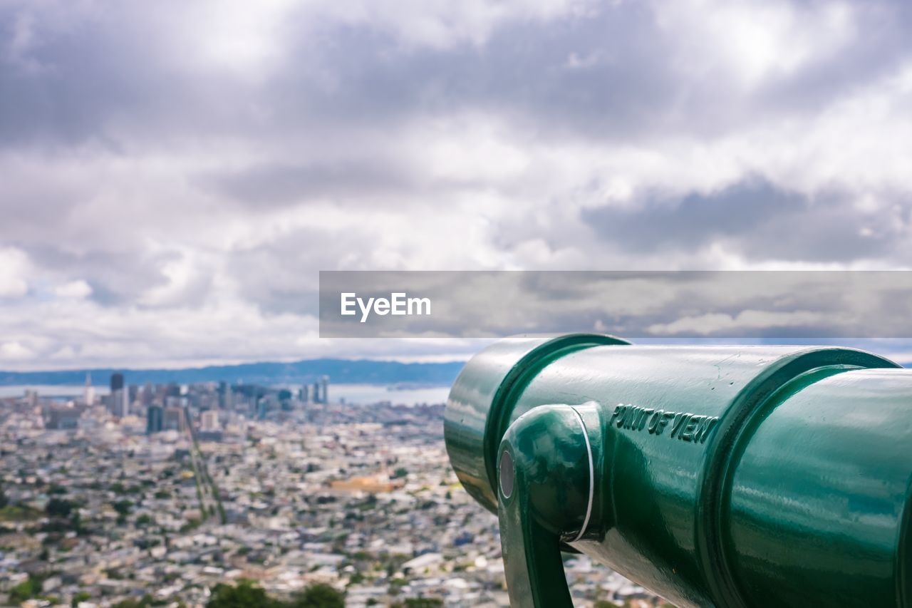 Close-up of telescope with city buildings in background