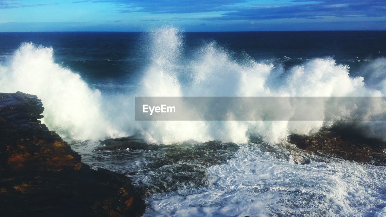 WAVES SPLASHING ON ROCKS AGAINST SKY