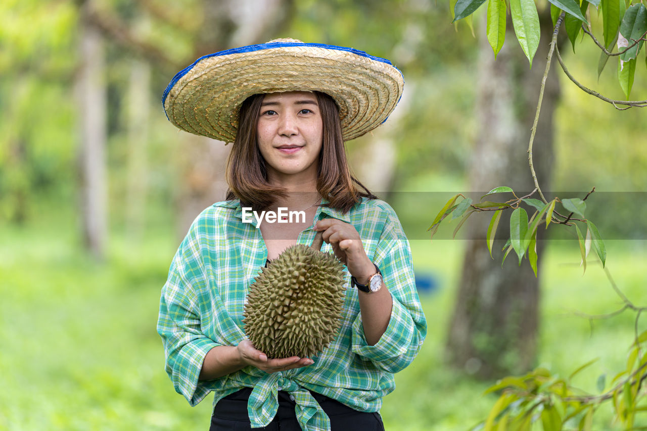 PORTRAIT OF WOMAN WITH HAT HOLDING PLANTS