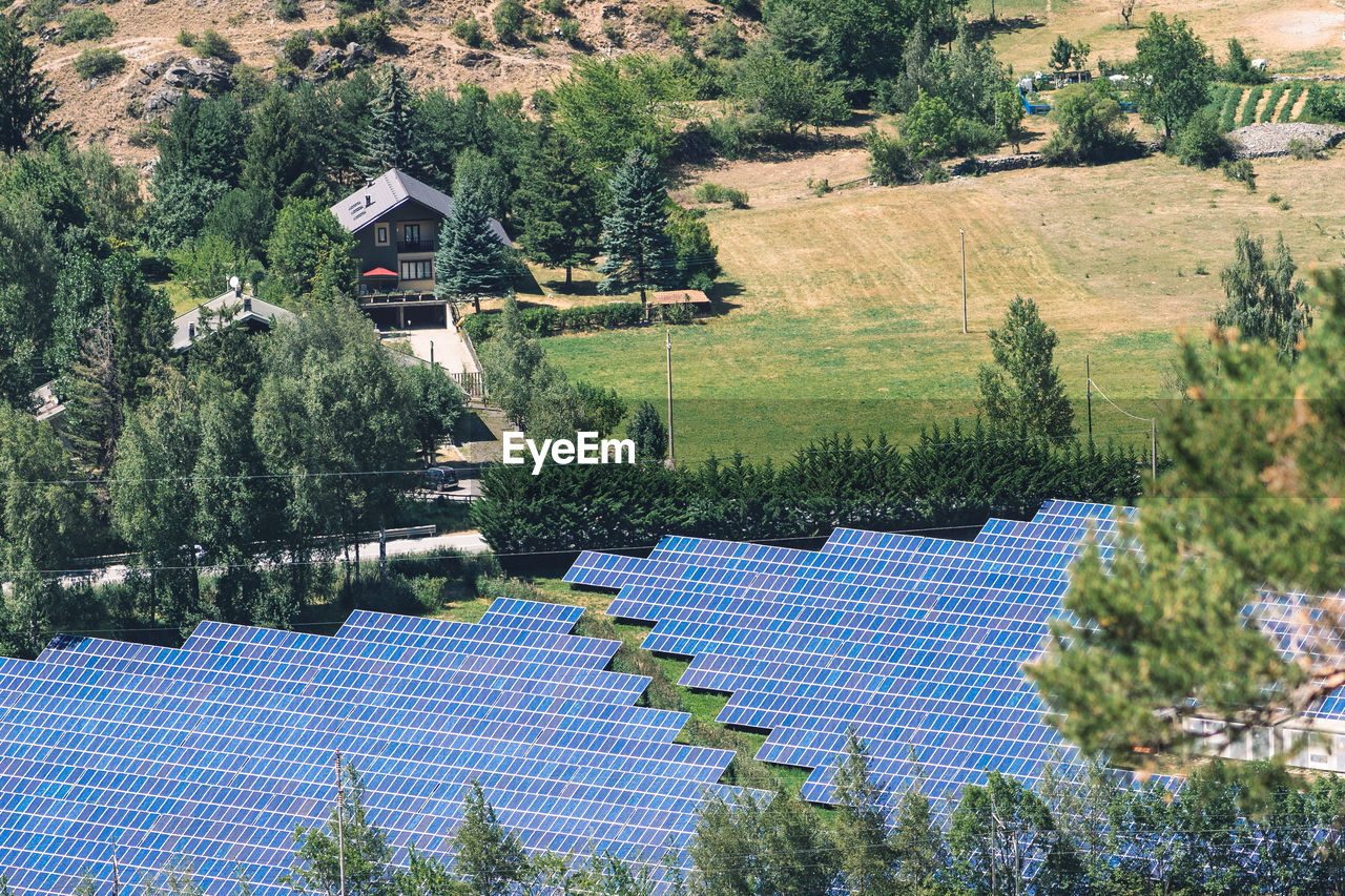 Aerial view of solar panels in the field in the countryside with house and cultivation on background