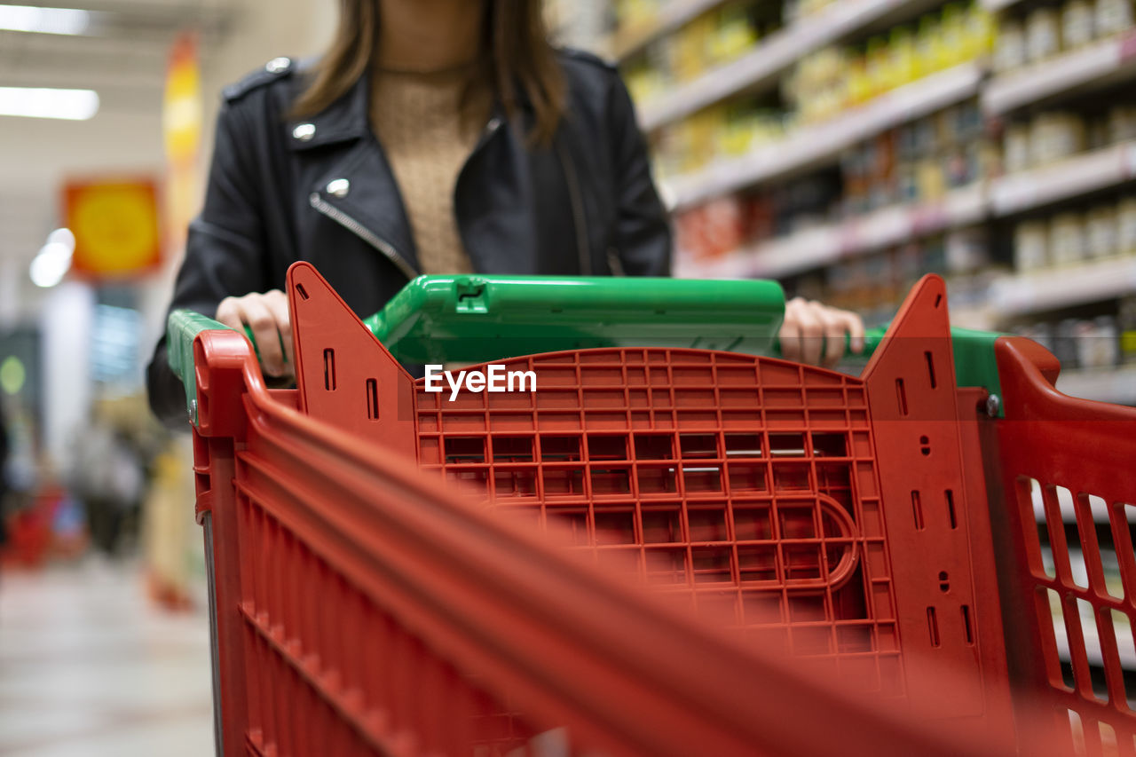 Woman carrying a red shopping cart in the supermarket.