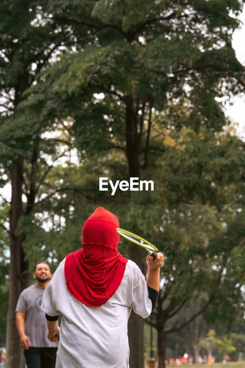 Asian family playing badminton in the park. woman in hijab, view from behind.