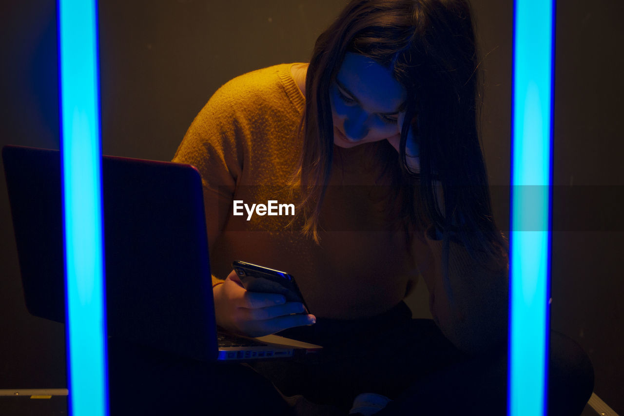 Woman using mobile phone and laptop while sitting in the dark