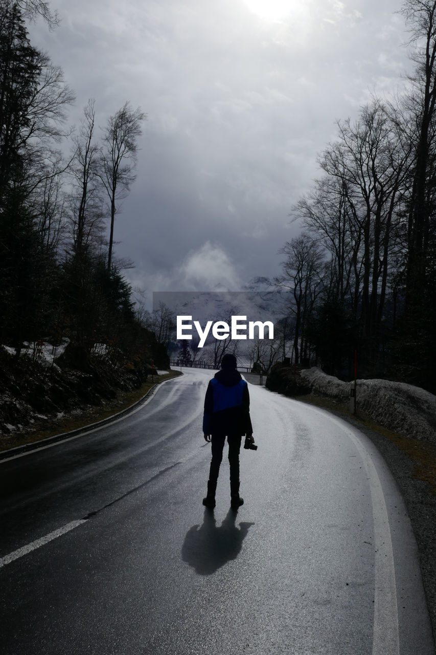 REAR VIEW OF MAN WALKING ON ROAD AMIDST TREES