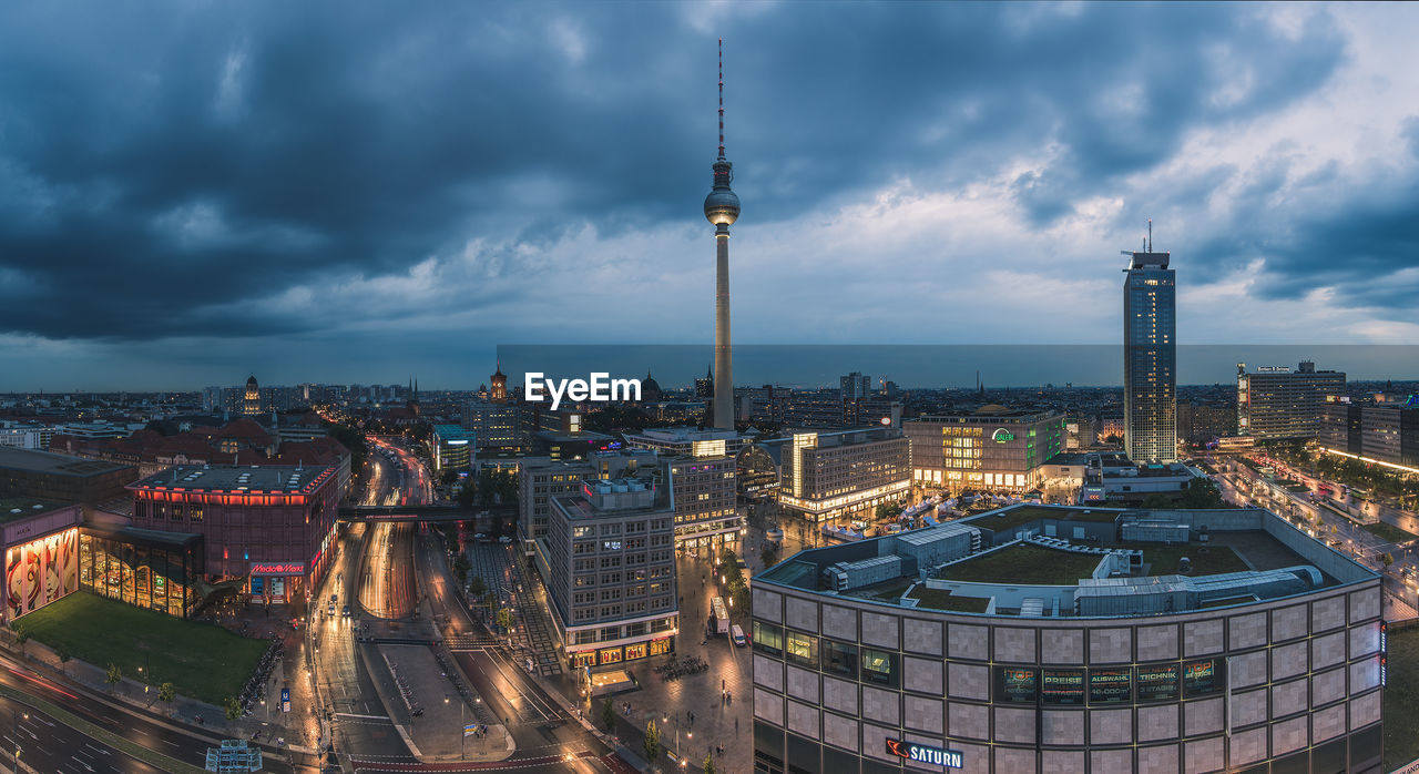 Fernsehturm in illuminated cityscape against cloudy sky at dusk