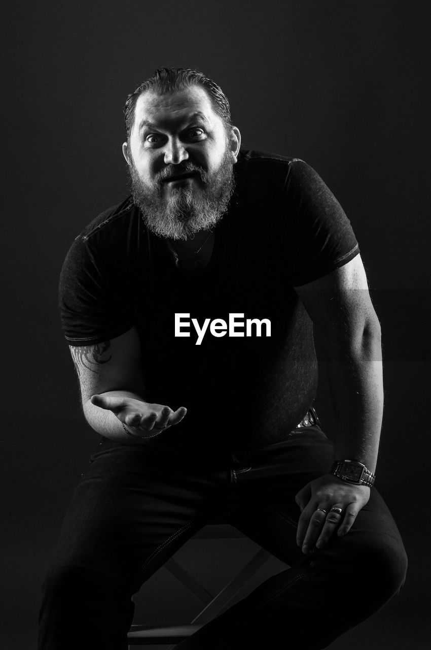 Portrait of mid adult man gesturing while sitting against black background