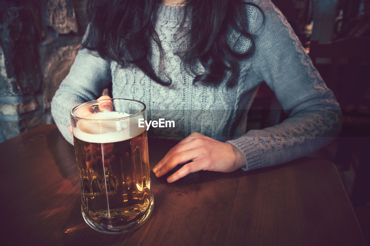 MIDSECTION OF WOMAN DRINKING GLASS WITH BEER ON TABLE