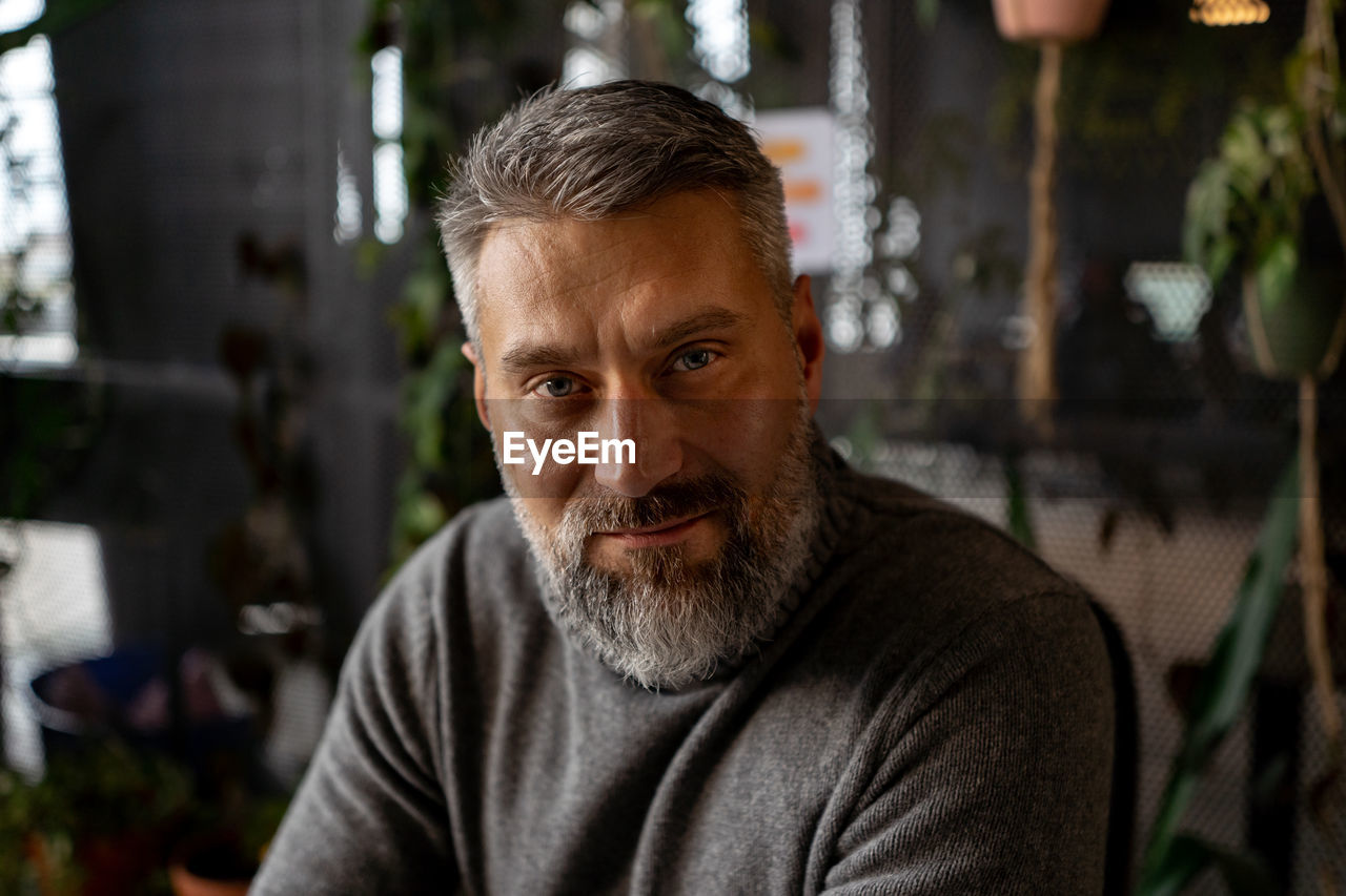 Portrait view of the attractive senior guy is posing to the camera at green plants office