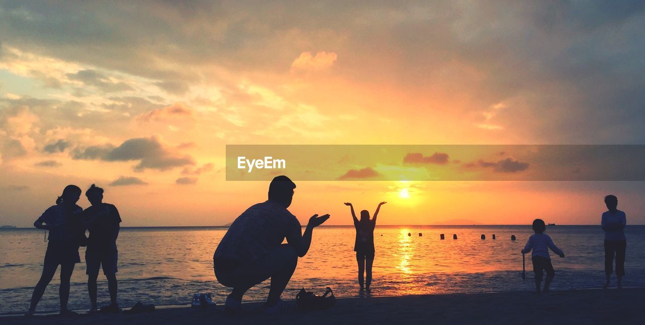 Silhouette people at beach against sky during sunset