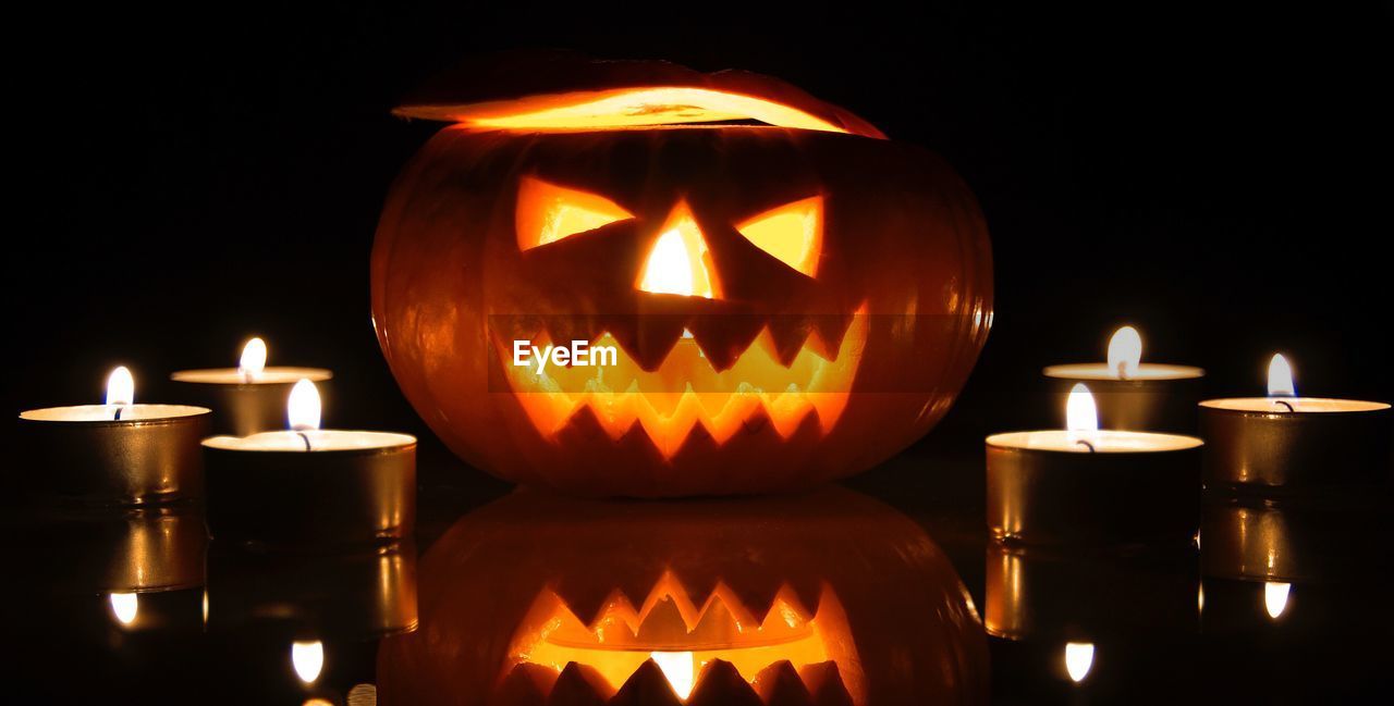 Illuminated jack o lantern and tea light candles against black background