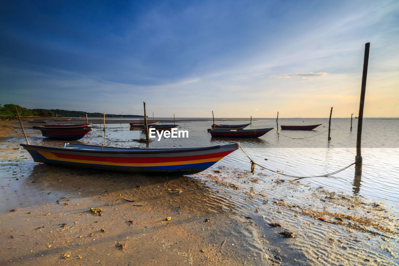 BOATS MOORED ON BEACH AGAINST SKY DURING SUNSET