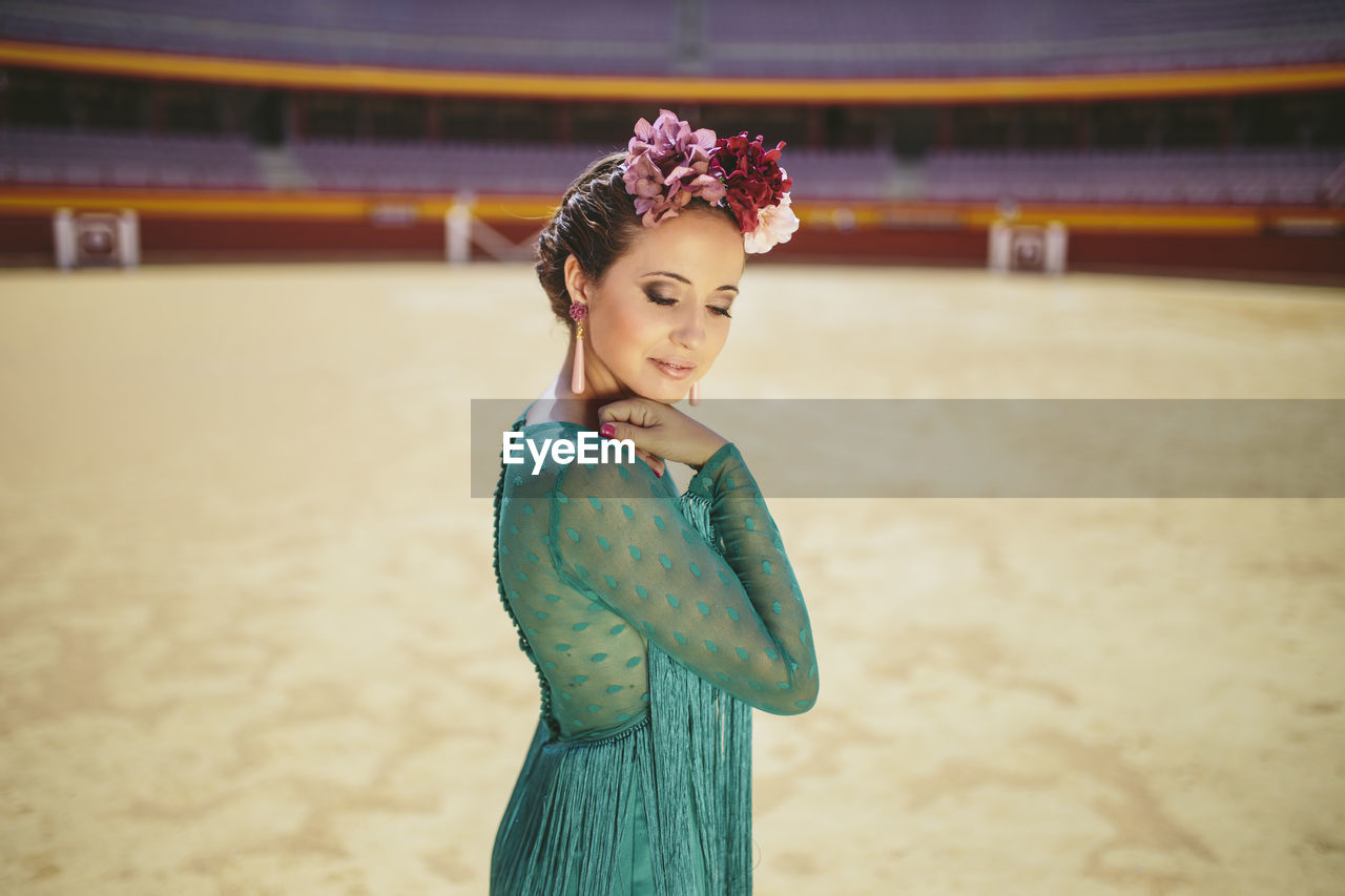 Flamenco dancer wearing blue dress and flowers posing while standing in bullring