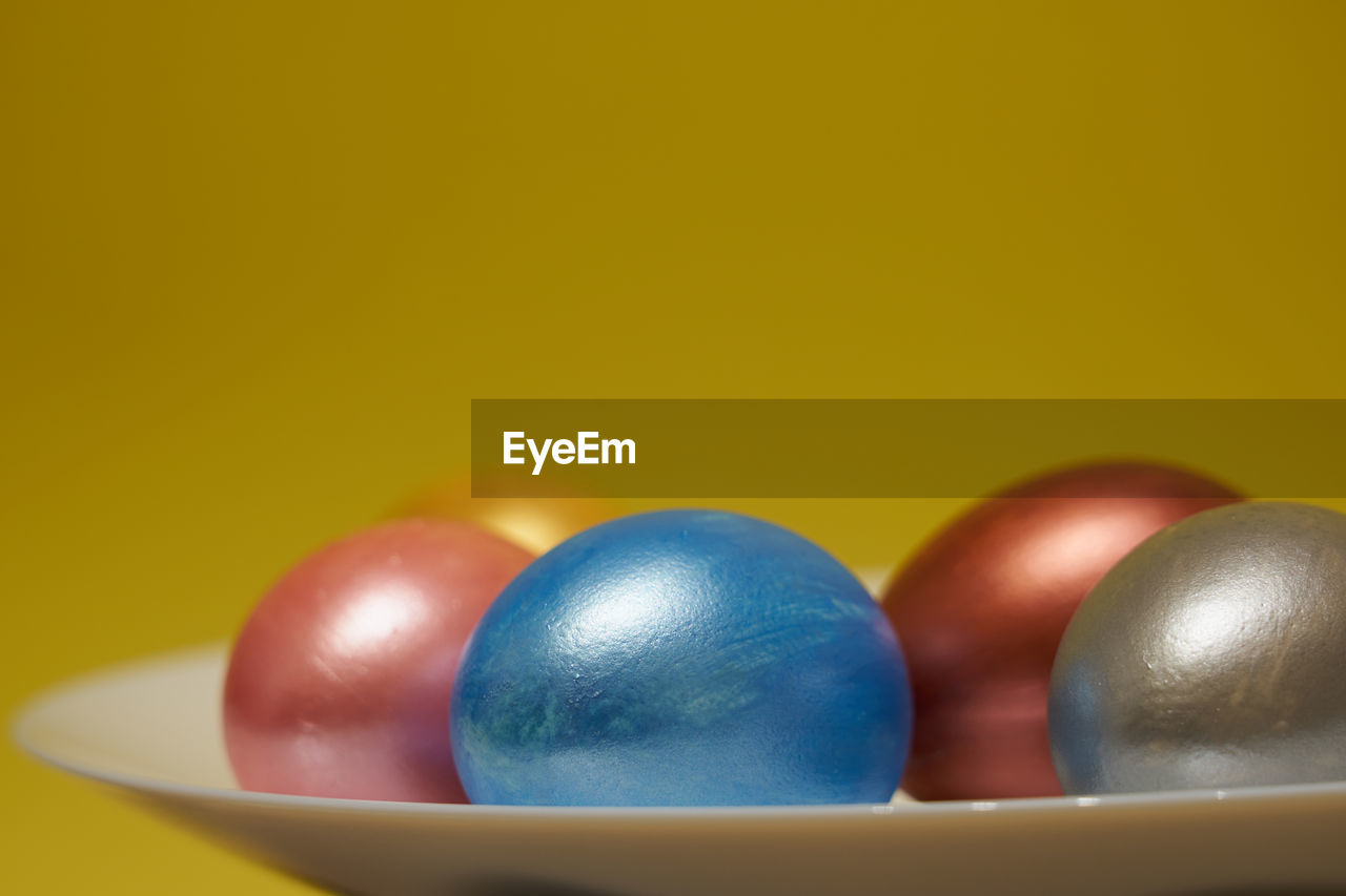 Painted eggs on a white plate with a yellow background.