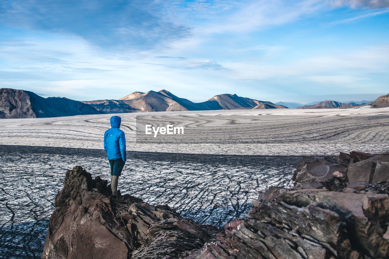 Rear view of man standing on cliff against landscape during winter